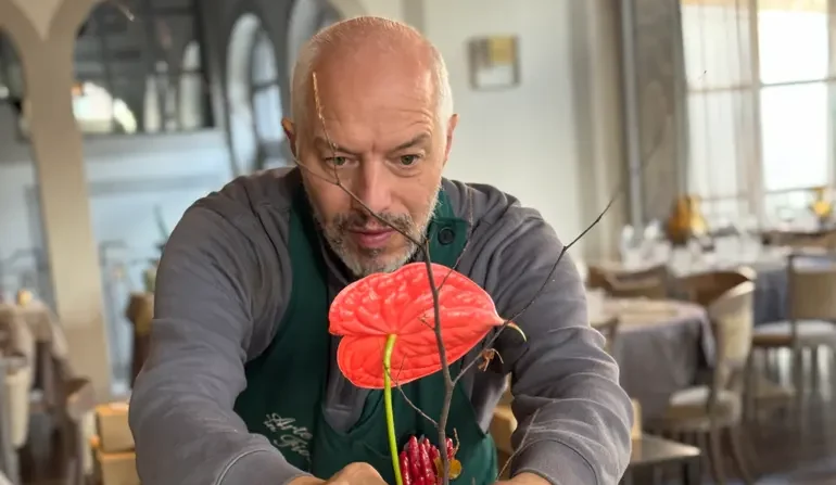 Fiorista sistema una composizione floreale con anthurium rosso su un tavolo apparecchiato per un matrimonio